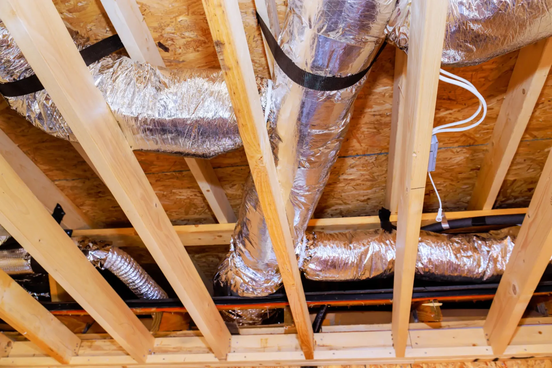 Exposed ceiling with wooden beams and insulated ductwork in a building under construction.