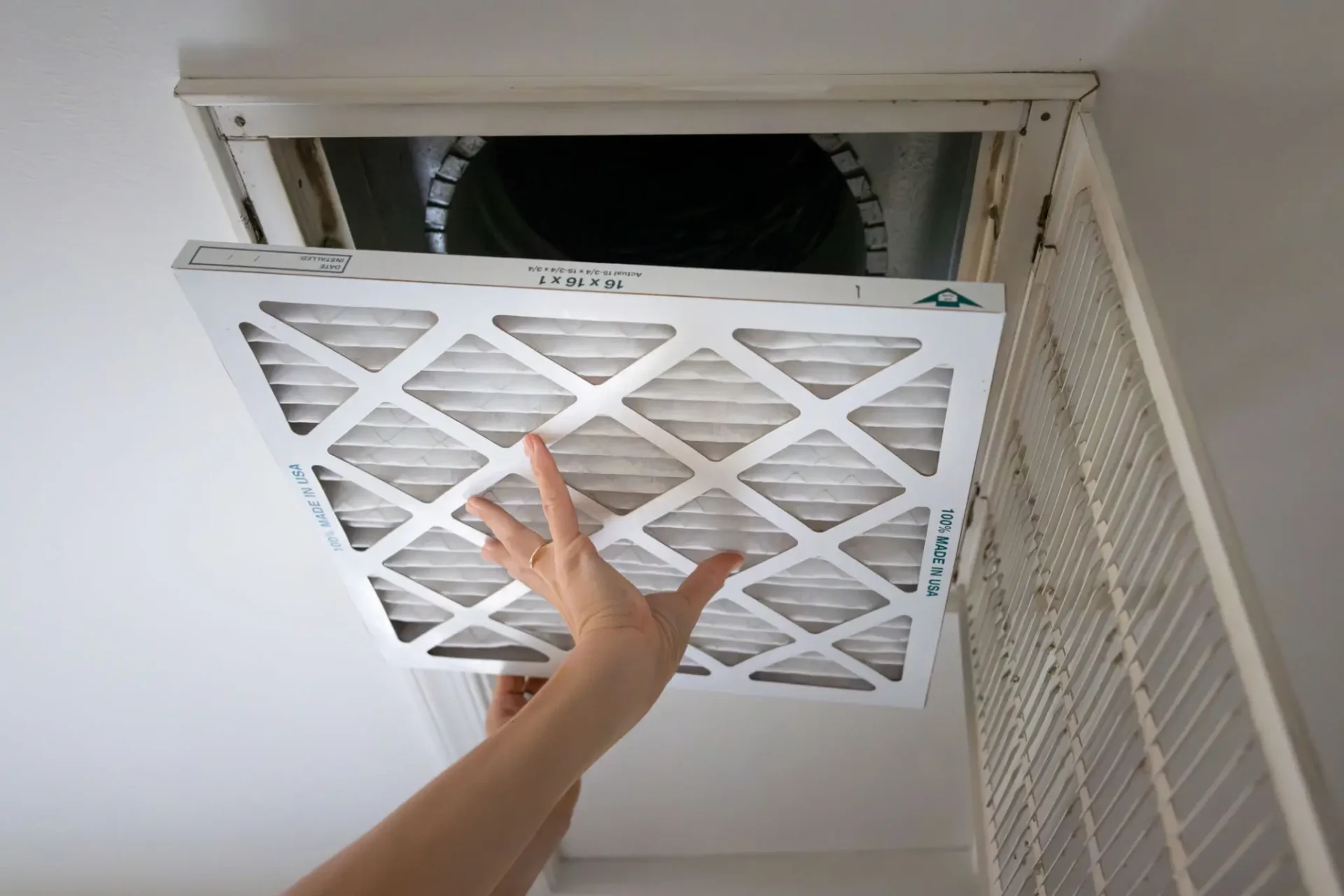 Hand removing a ceiling air filter from an air vent.