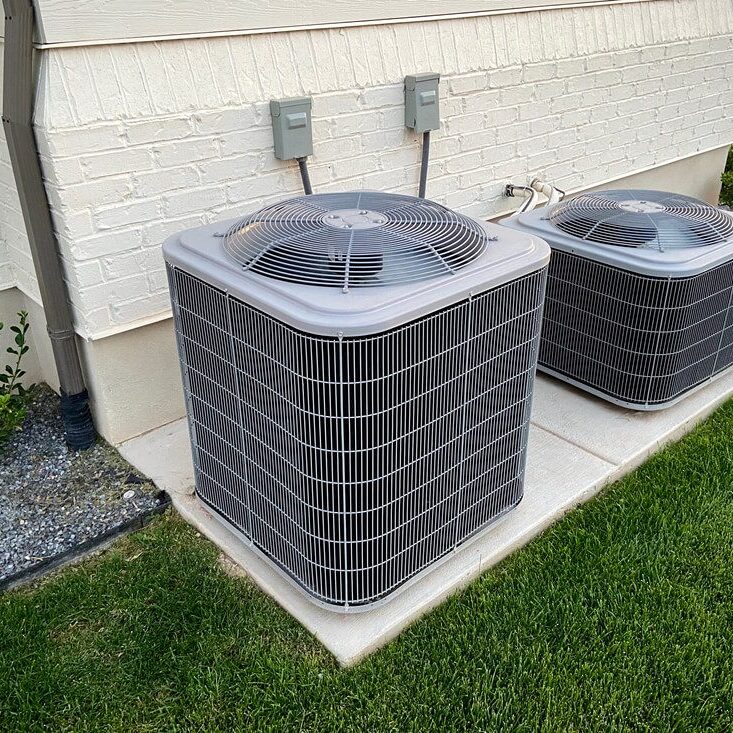 Two outdoor air conditioning units installed on a concrete slab beside a building.
